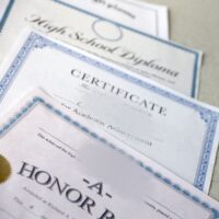 A honor roll recognition, certificate of achievement and high school diploma lies on table. Education documents close up