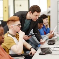 Vibrant side view portrait of male teacher helping student using computer in college classroom, copy space